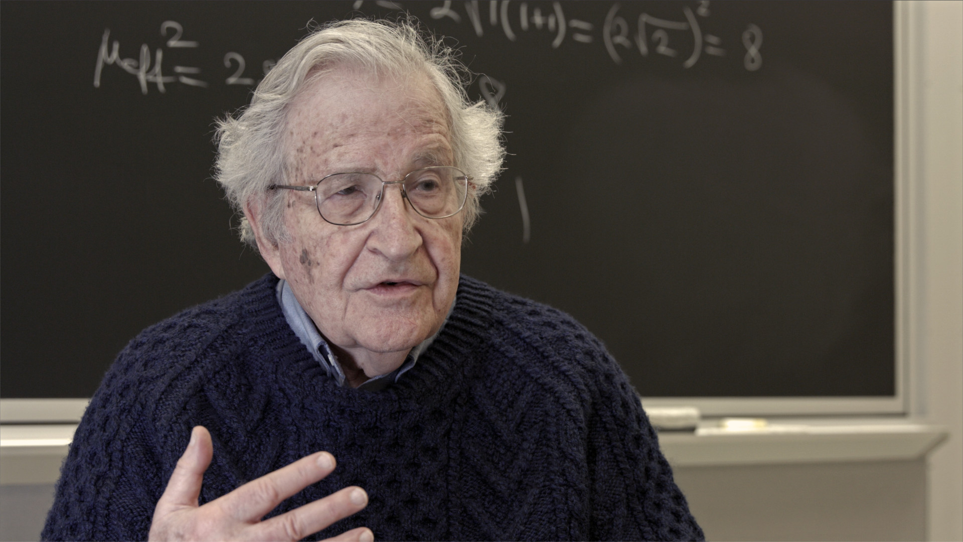 Noam Chomsky Disparity Film Still, Noam Chomsky in front of blackboard
