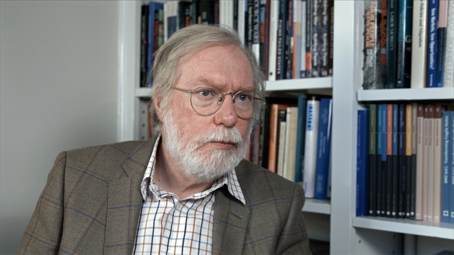 Disparity Film still, Sir Paul Collier in front of bookshelf